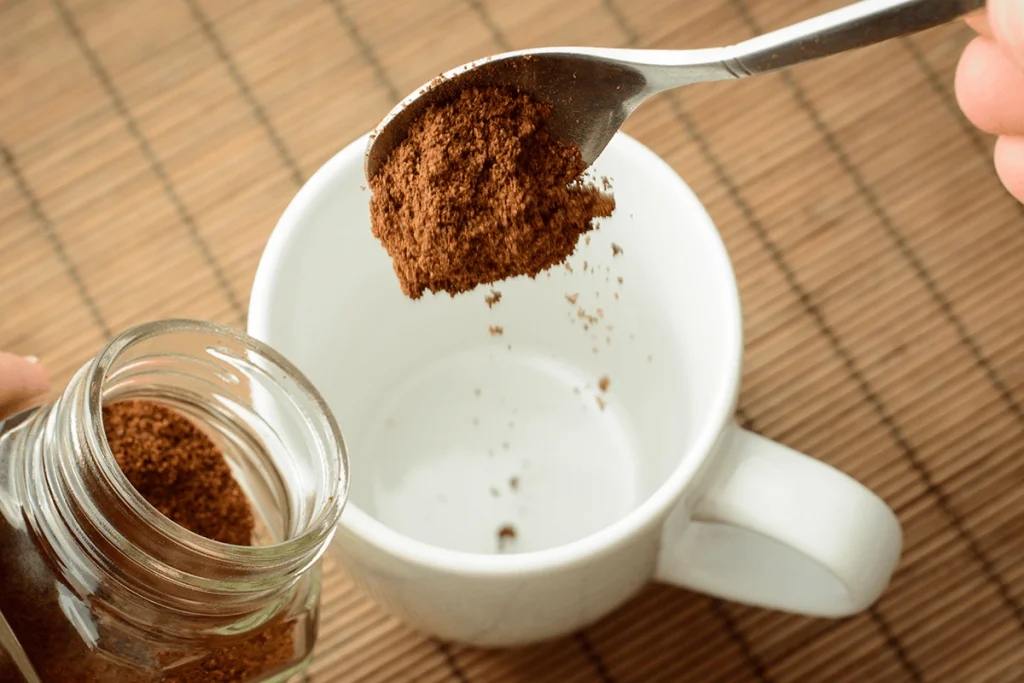 A spoonful of instant coffee being poured into a white mug, highlighting the robust and full-bodied flavor of Robusta used in instant and espresso blends.