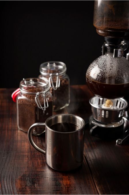 Immersion Coffee Brewing: Techniques, Equipment & Flavor Mastery 19 Syphon coffee maker brewing coffee with jars of coffee grounds and a metal mug on a wooden table.