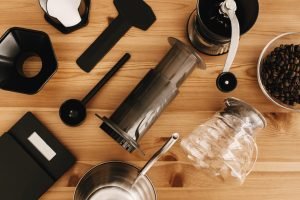 Máy pha cà phê AeroPress và nhiều phụ kiện pha cà phê khác trên bàn gỗ.