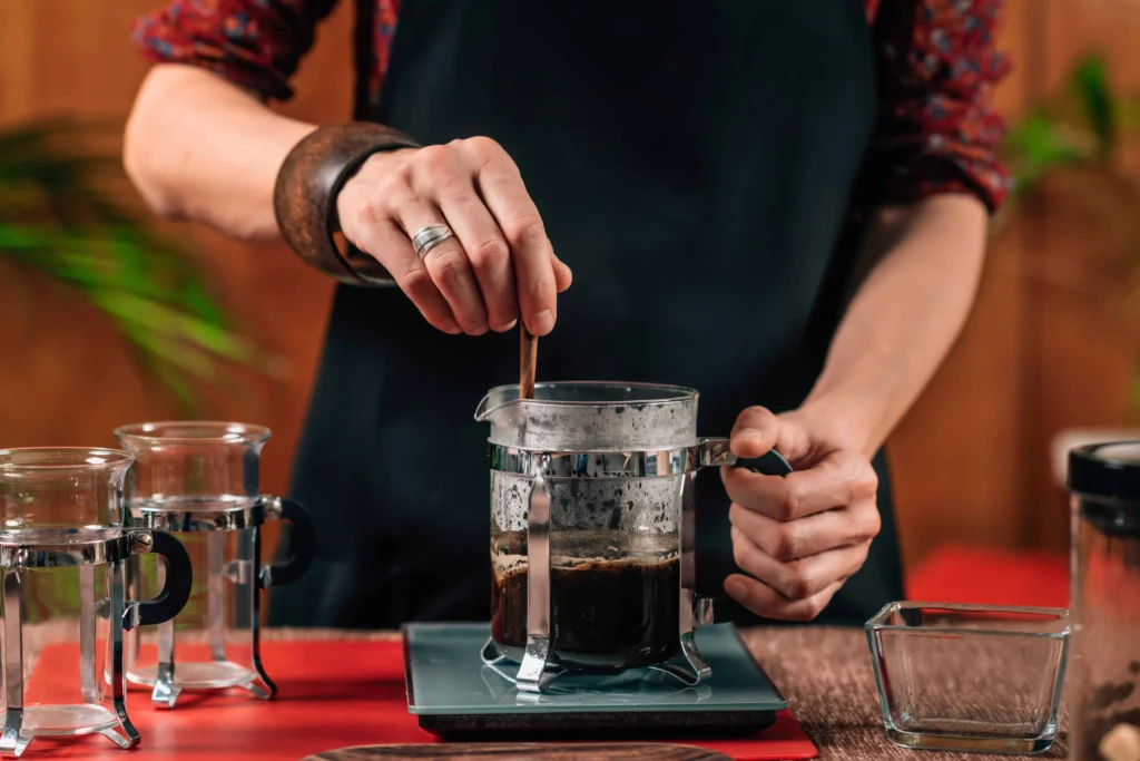 Immersion Coffee Brewing: Techniques, Equipment & Flavor Mastery 28 A barista gently stirs freshly brewed coffee in a French press using a wooden stirrer.