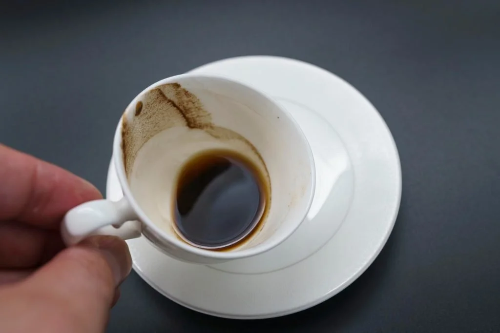 A white coffee cup with coffee grounds at the bottom on a saucer
