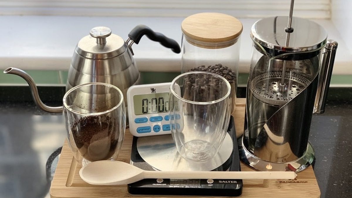 Coffee brewing setup with a French Press, gooseneck kettle, coffee beans, digital timer, and glass mugs on a wooden tray.