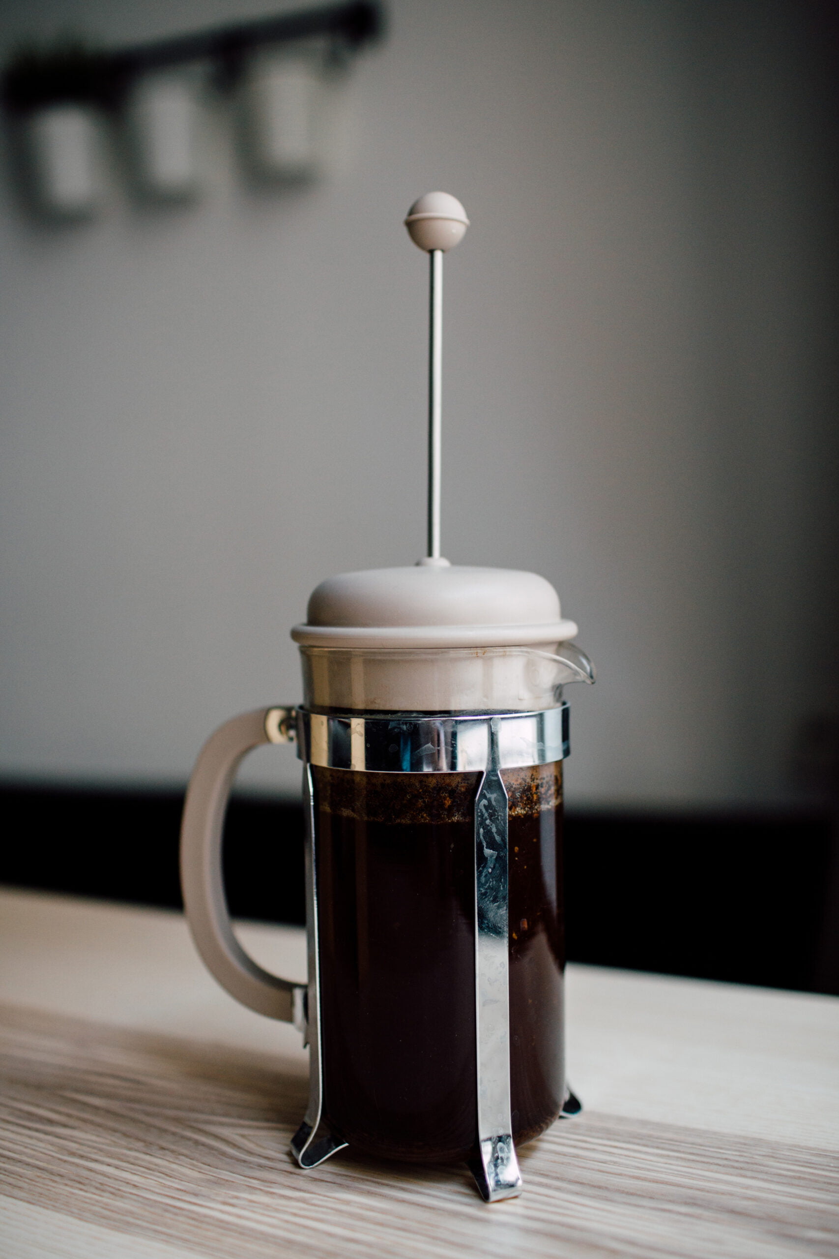 A French press sits on a wooden table, filled with freshly brewed coffee.