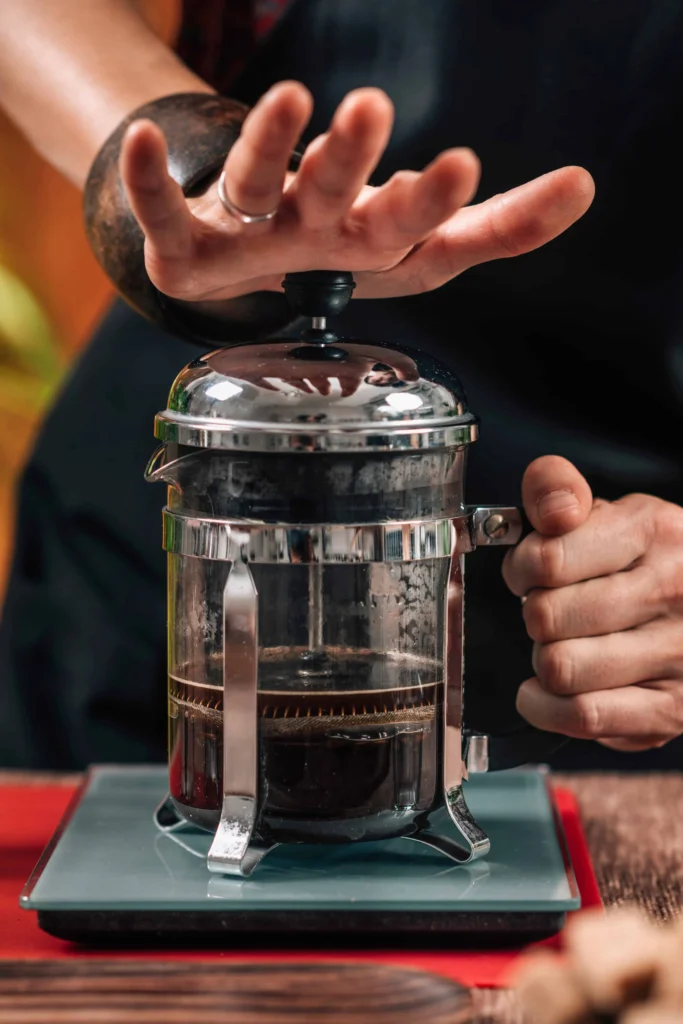 The Ultimate Guide to 12 Cup French Coffee Press Brewing 17 A barista gently places their hand atop a French press, ready to plunge and brew a perfect cup of coffee.