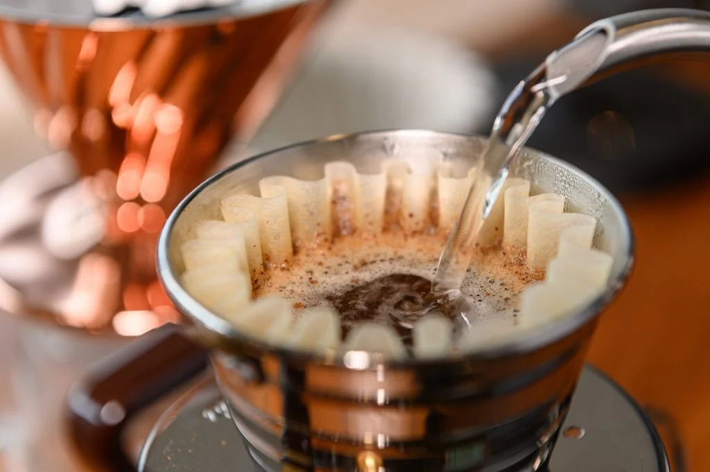 A detailed view of a Kalita pour over brewer with water cascading over fresh coffee grounds.