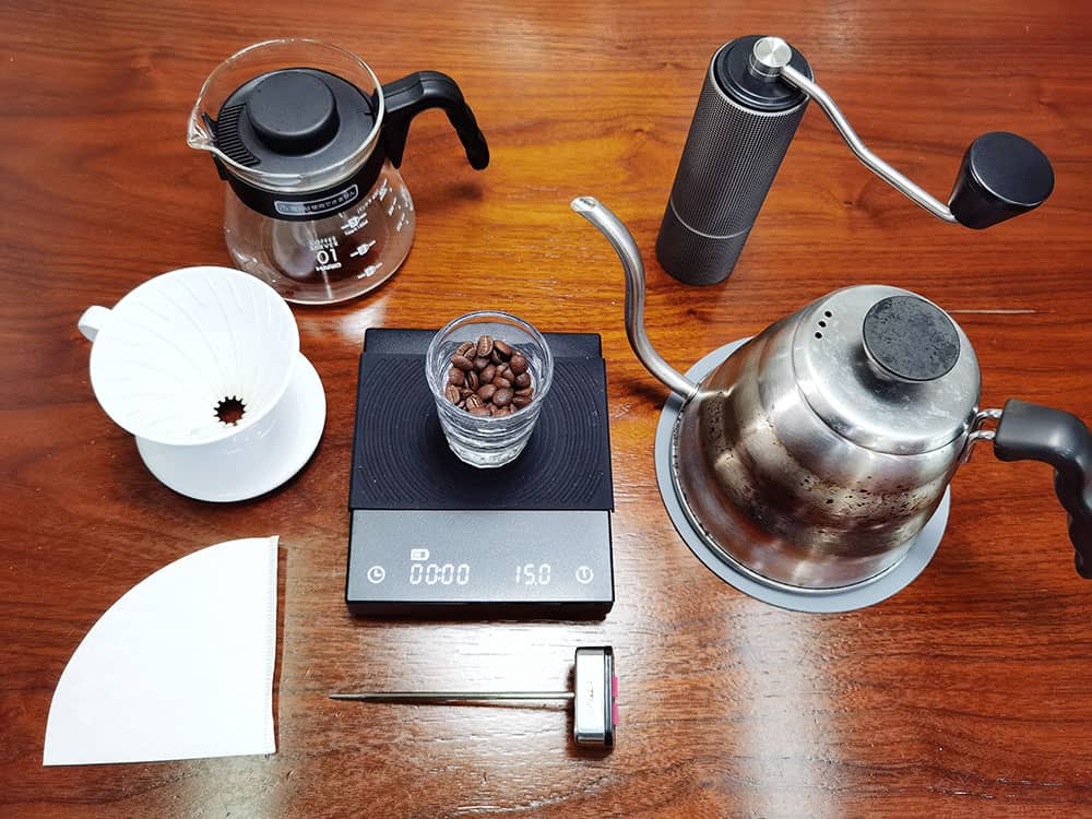 Bộ dụng cụ pha cà phê pour-over hoàn chỉnh với ấm đun, máy xay và bình chứa trên bàn gỗ.