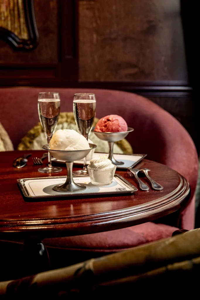 Một chiếc bàn tại Le Procope với hai ly champagne, một muỗng kem vani, một muỗng sorbet quả mâm xôi và một chiếc bánh cupcake.