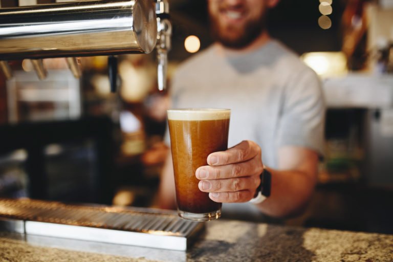 What is Nitro Coffee? The Science Behind This Creamy, Next-Level Cold Brew 7 A barista smiles as he holds a freshly poured glass of nitro cold brew coffee.