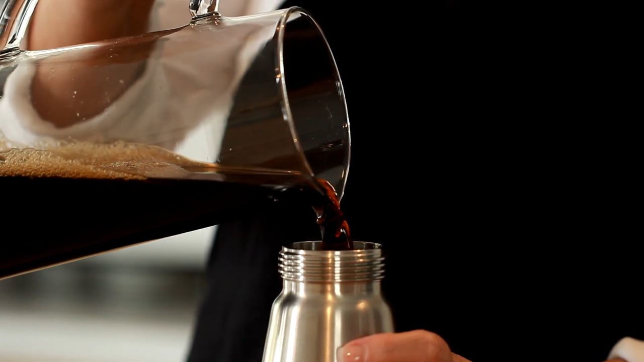 Pouring cold brew coffee from glass carafe into stainless steel bottle