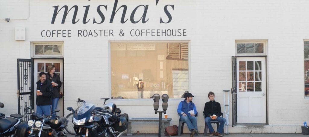 Alexandria's Ultimate Cortado Cafe & Coffee Shop Guide 2025 9 White facade of Misha's Coffee Roaster & Coffeehouse with black lettering, showing customers relaxing outside, motorcycles parked in front, and classic wrought-iron doors and windows in Old Town Alexandria.