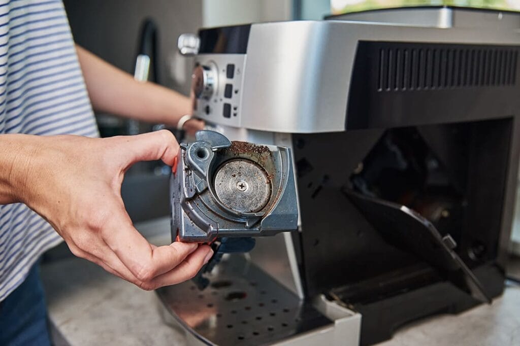 The Ultimate Coffee Maker Guide: From Basics to Pro Tips 2025 20 Person inspecting and cleaning dirty brew unit of espresso machine, showing common maintenance issues and buildup of coffee residue