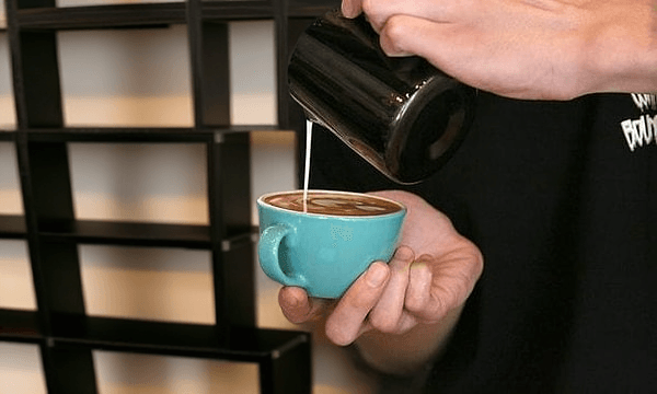 The Ultimate Guide to Flat White Cups, Flat White Mugs & Finding the Best Flat White Cups 7 Barista pouring steamed milk from black pitcher into turquoise flat white cup to create latte art