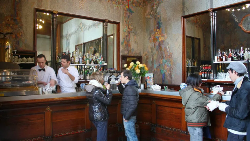 Espresso vs. Cappuccino: The 30-Second Trick to Picking the PERFECT Brew Every Time 8 Traditional Italian espresso bar with elegant wooden counter, uniformed baristas serving customers standing at the bar, ornate wall decorations, and mirrors - showcasing the authentic standing ritual of Italian coffee culture