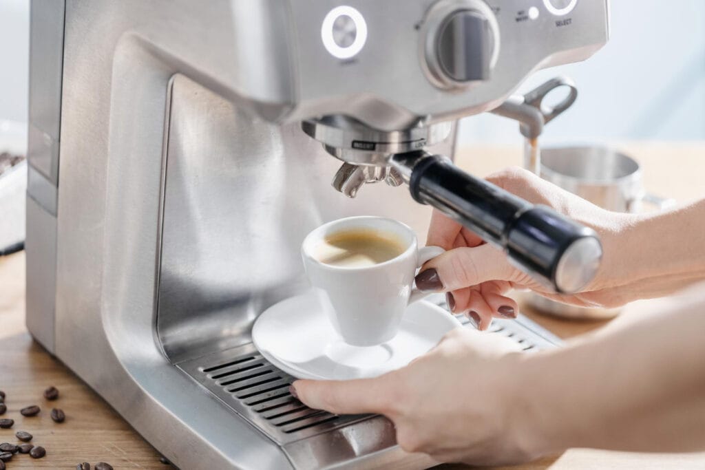 Person extracting espresso with a stainless steel home espresso machine using portafilter for café-quality coffee
