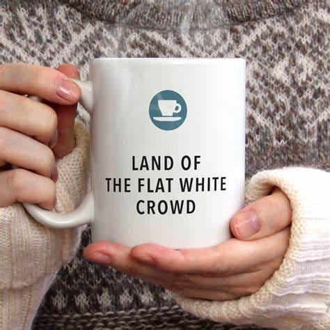The Ultimate Guide to Flat White Cups, Flat White Mugs & Finding the Best Flat White Cups 8 White ceramic mug with "Land of the Flat White Crowd" text and blue coffee cup logo held by person in knitted sweater