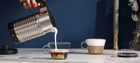 Aeroccino milk frother pouring freshly frothed milk into an espresso cup on marble countertop against blue background