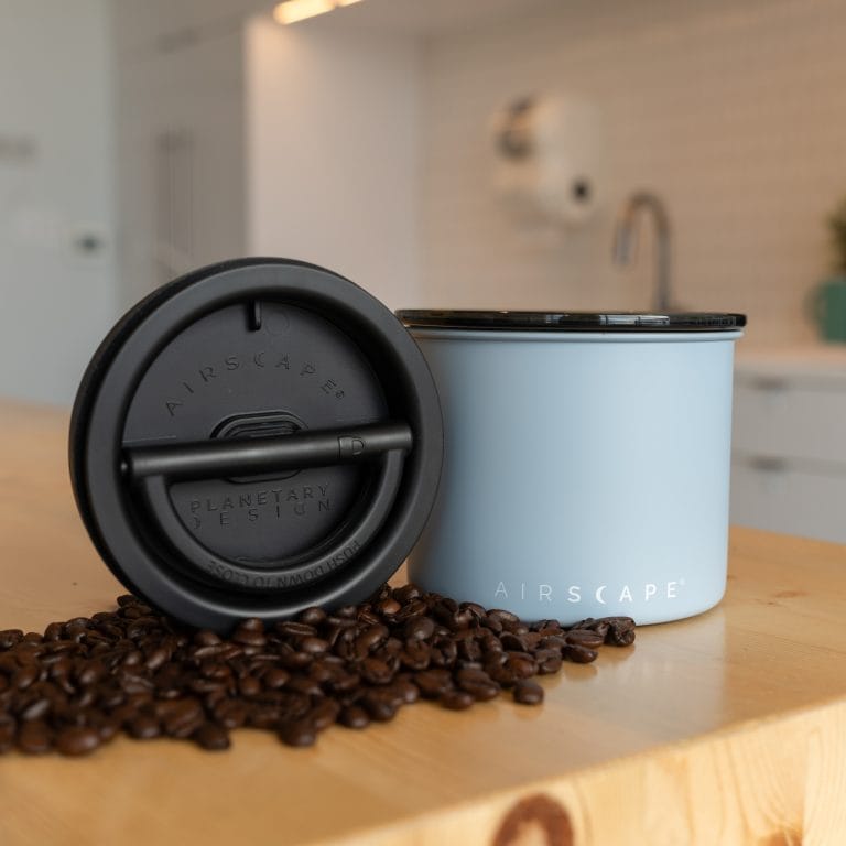 Airscape Coffee Canister in light blue with black airtight lid and coffee beans on wooden counter