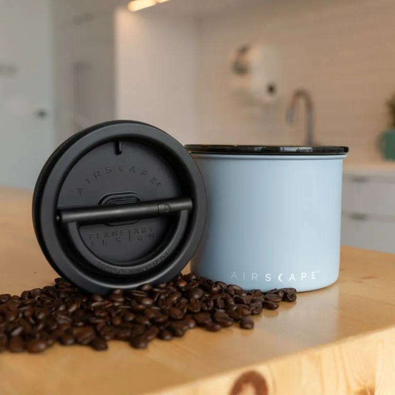 Airscape Coffee Canister in light blue with black airtight lid and coffee beans on wooden counter