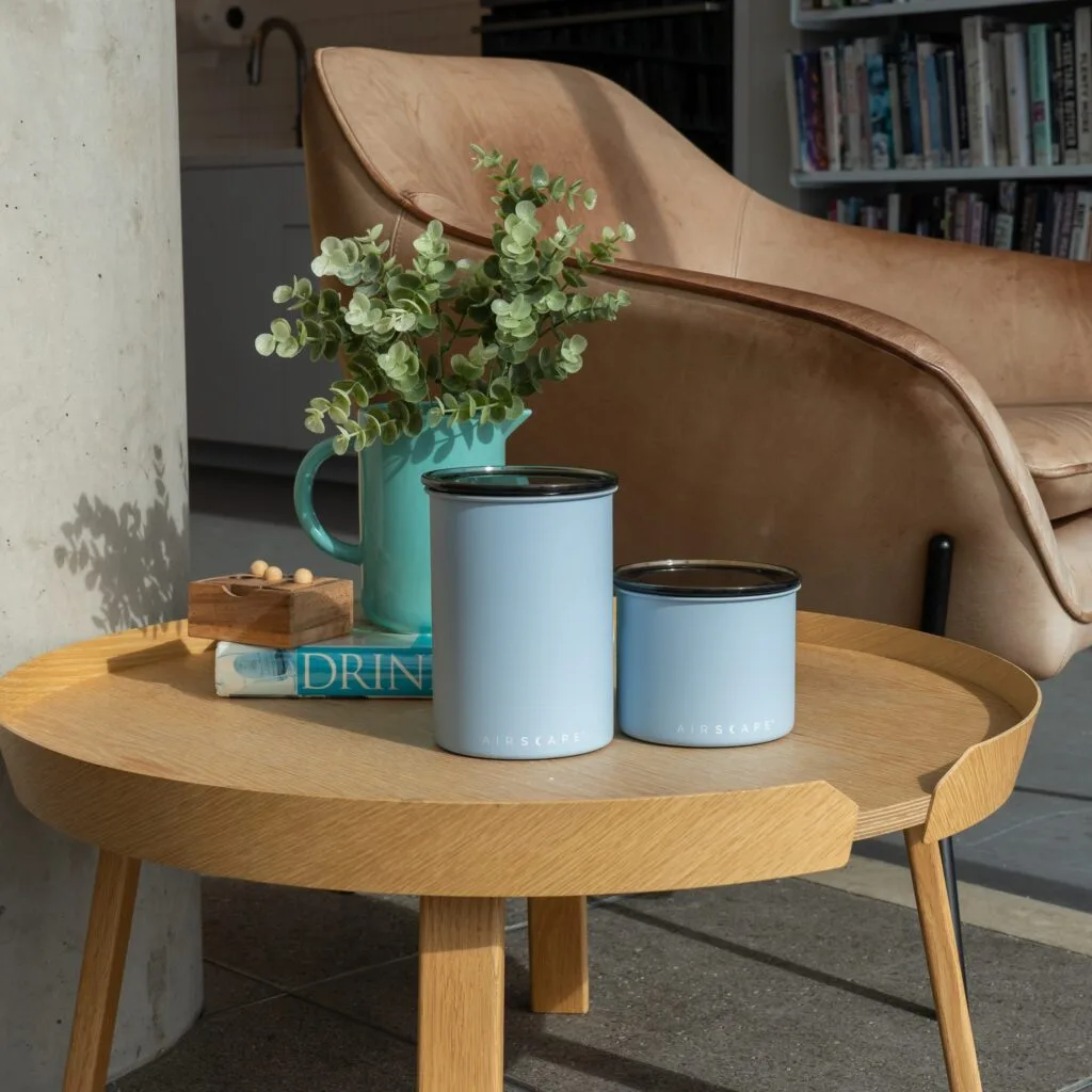 Airscape coffee canisters in light blue displayed in stylish living space, showing how these storage containers preserve coffee freshness and flavor while complementing modern home decor