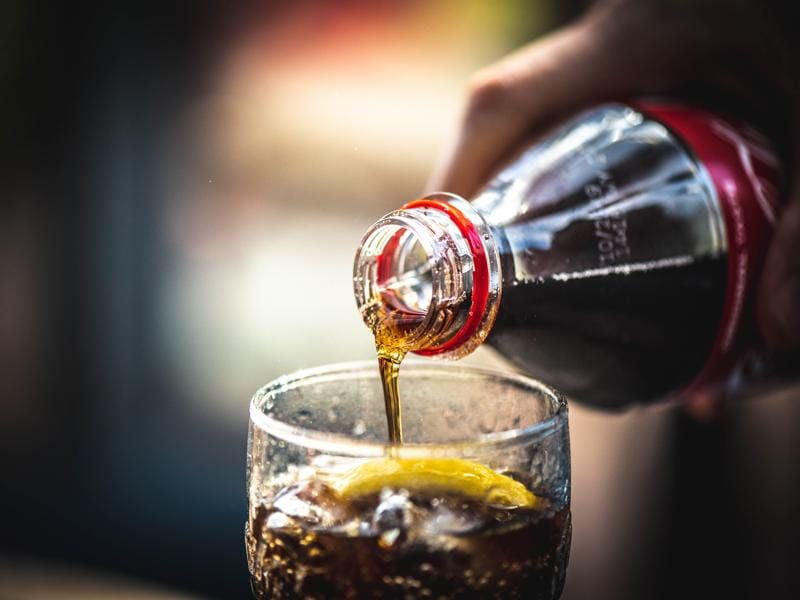 Caffeine Content in Soda Vs Coffee: Complete Comparison Guide 8 Pouring dark cola soda from bottle into glass with ice showing soda's caffeine content comparison