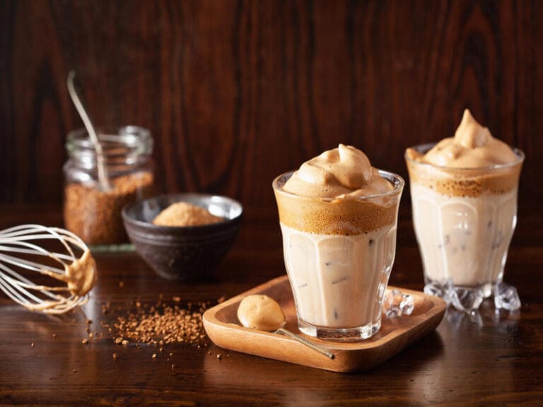 7 Copycat Starbucks Homemade Recipes in Minutes 5 Two glasses of whipped coffee on ice with ingredients and whisk on wooden table, homemade Starbucks copycat recipe