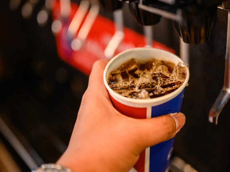 Caffeine Content in Soda Vs Coffee: Complete Comparison Guide 7 Hand holding fizzy cola soda drink with ice bubbles showing soda's caffeine content