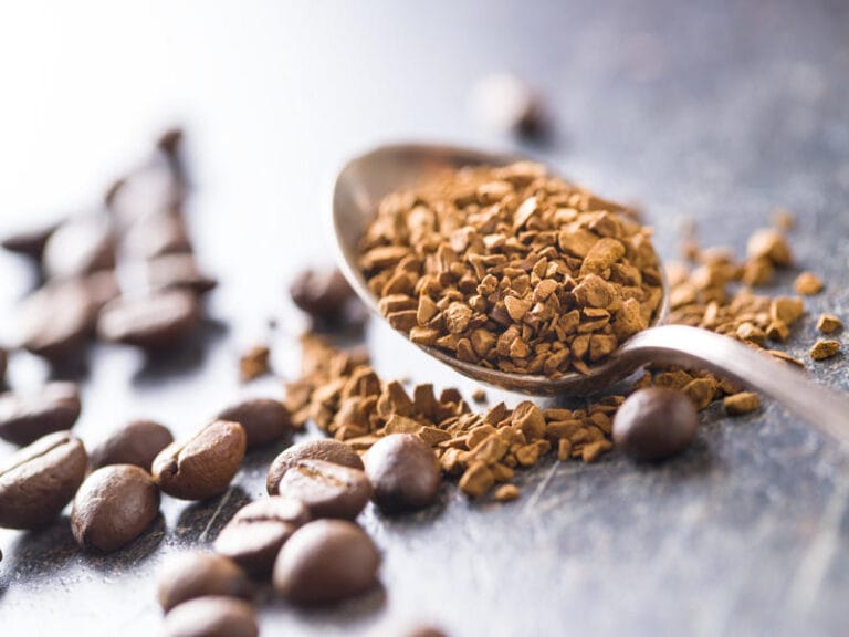 Granulated coffee in wooden spoon with whole coffee beans showing texture and processing differences