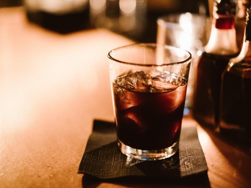 How Do Americano Vs Macchiato Differ in Caffeine Taste and Strength? 11 Glass of Americano coffee served on the rocks with ice cubes on a dark napkin