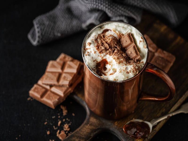 Mocha hot chocolate with whipped cream and chocolate shavings in copper mug with chocolate bars