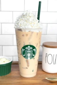 Venti iced white mocha from Starbucks topped with whipped cream in a clear plastic cup with green straw
