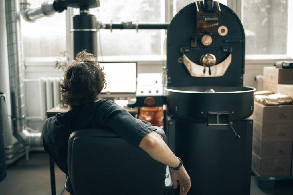 Man monitoring coffee roasting process in front of professional coffee roaster machine in a roasting facility